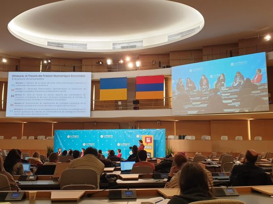 Photographie de l'événement 'Rencontres Régionales Hinaura' le 19 décembre à Lyon, montrant un amphithéâtre moderne avec des participants assis devant des ordinateurs portables. À l'avant, un écran affiche la session en cours avec des panneaux 'La Région' en arrière-plan. Des drapeaux français et de l'Union Européenne sont également visibles. En haut, un texte liste cinq missions structurantes liées à France Numérique Ensemble.